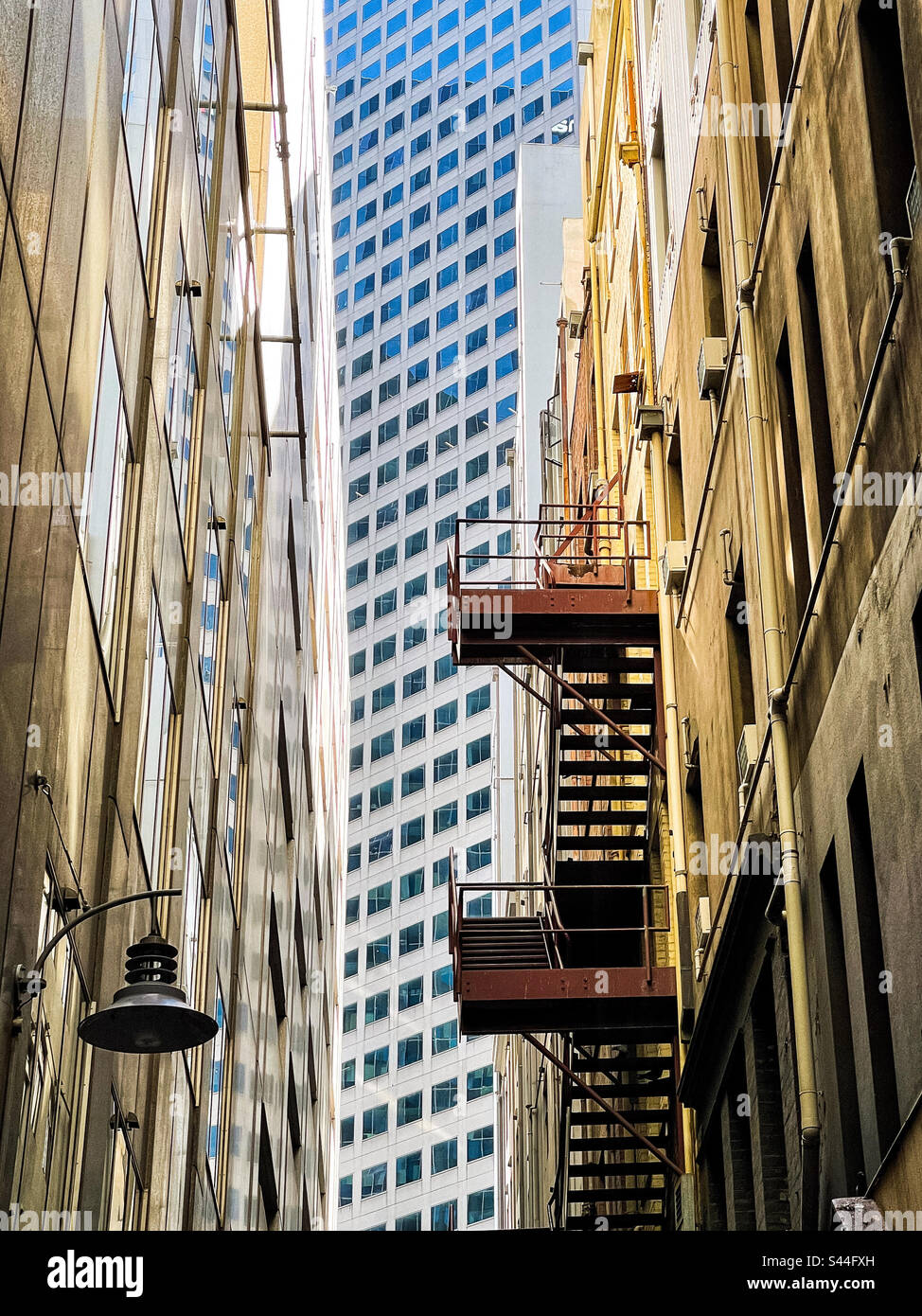 Nebeneinander. Alte Gebäude mit Feuertreppe in einer schmalen Gasse vor dem modernen Wolkenkratzer in der Mitte am Ende der Gasse in Melbourne, Victoria, Australien. Ansicht aus niedrigem Winkel. Stockfoto