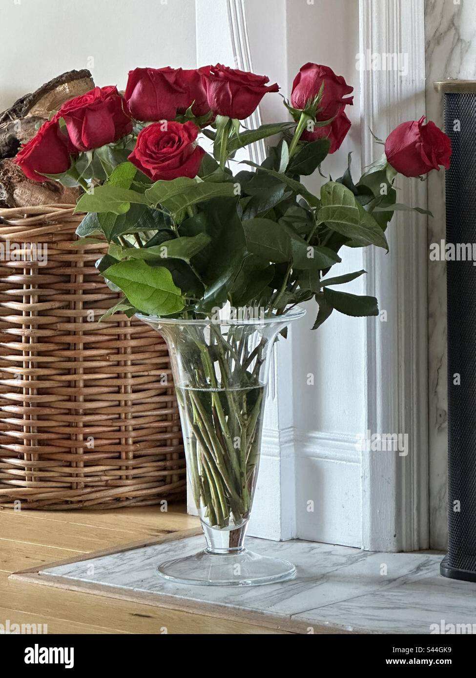 Ein Haufen roter Rosen in einer Glasvase auf dem Marmorboden vor einem Kamin - Smartphone-aufgenommenes Stockfoto