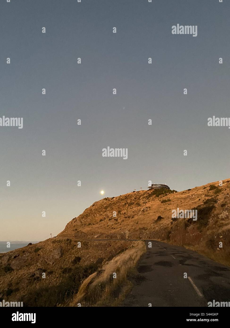 Der Mond erhebt sich über einen Hügel mit einer leeren Straße, die zu ihm führt. Stockfoto