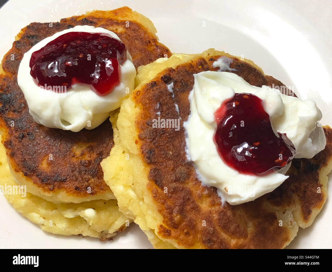 Zwei ukrainische Syrniki (Käsepfannkuchen) werden auf traditionelle Weise mit Sauerrahm und Marmelade serviert. Stockfoto