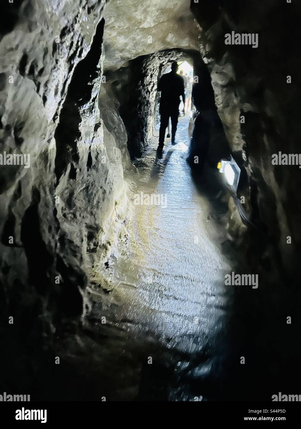 Der silhoutierte Hintern eines Mannes, der durch einen gruseligen dunklen Tunnel zum Licht geht - Smartphone-aufgenommenes Stockfoto