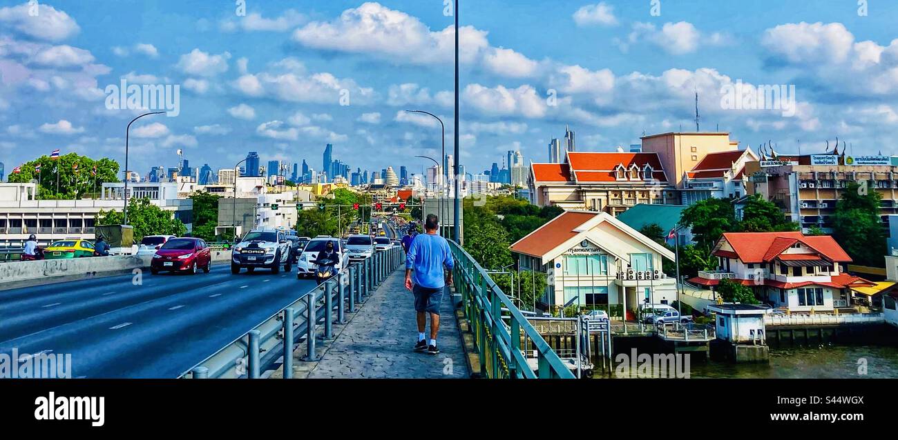 Mann geht über die Brücke über den Fluss Chao Phraya mit Blick auf Bangkok im Hintergrund - Smartphone-aufgenommenes Stockfoto