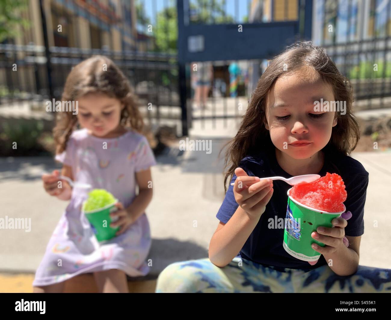 2 Mädchen essen rasiertes Eis draußen in der Sonne. Stockfoto