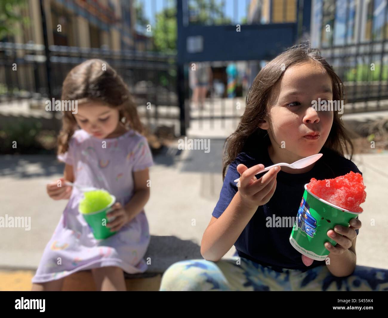 2 Mädchen essen rasiertes Eis draußen in der Sonne. Stockfoto