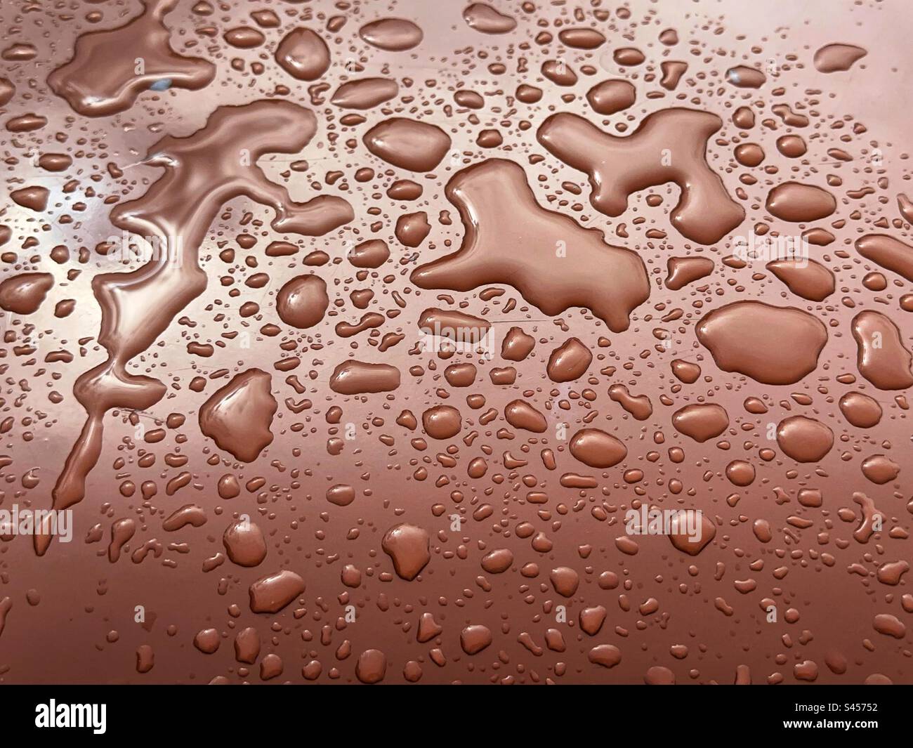 Wassertropfen auf einer glänzenden braunen Oberfläche nach einem Regenschauer. Hintergründe. Stockfoto