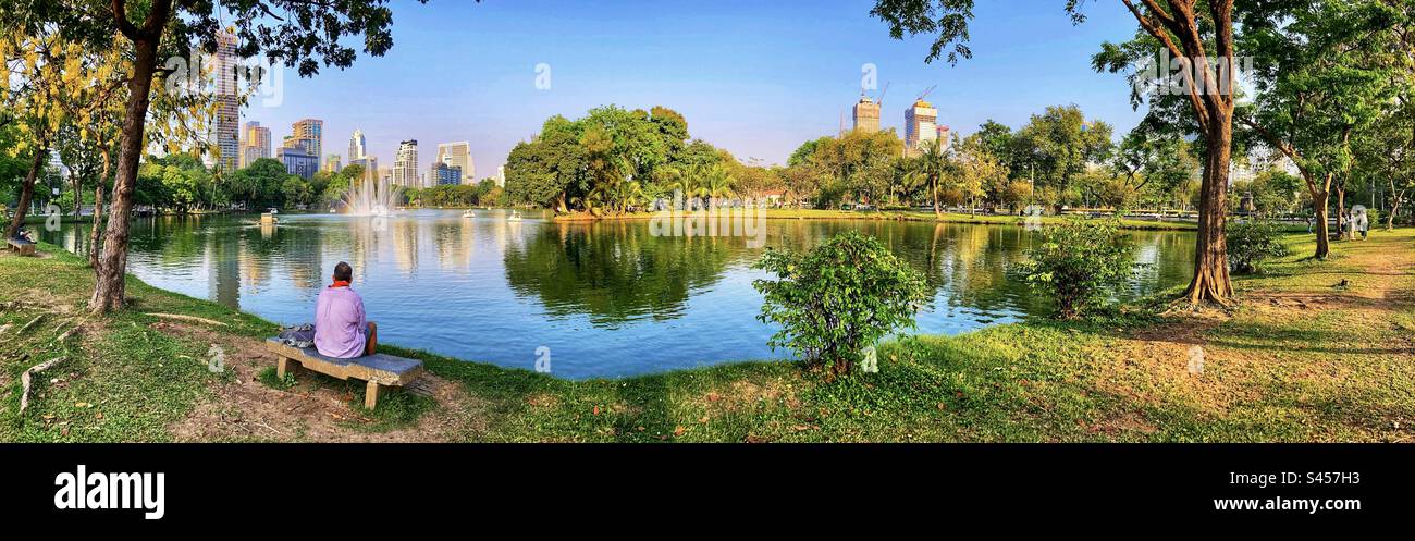 Panoramablick auf den Mann, der auf einer Bank im Lumpini Park Bangkok Thailand sitzt Stockfoto