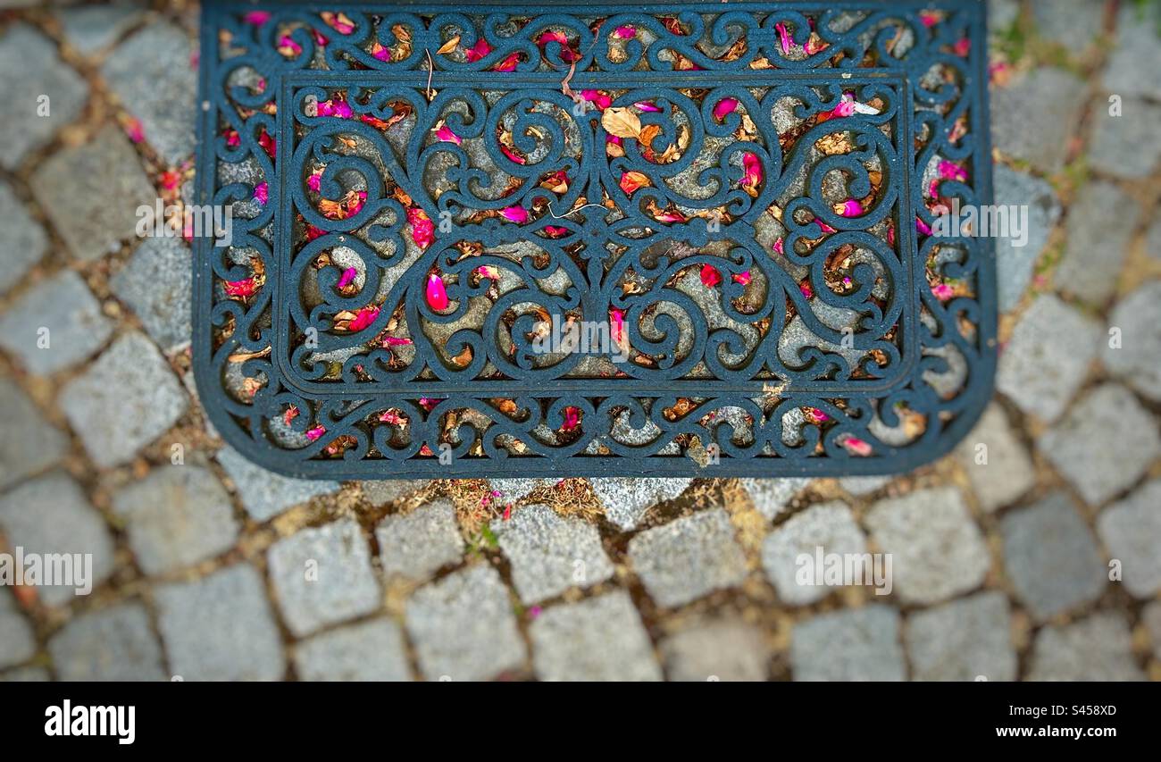Schwarze Türmatte mit pinkfarbenen Blütenblättern auf einem steinernen Hof Stockfoto