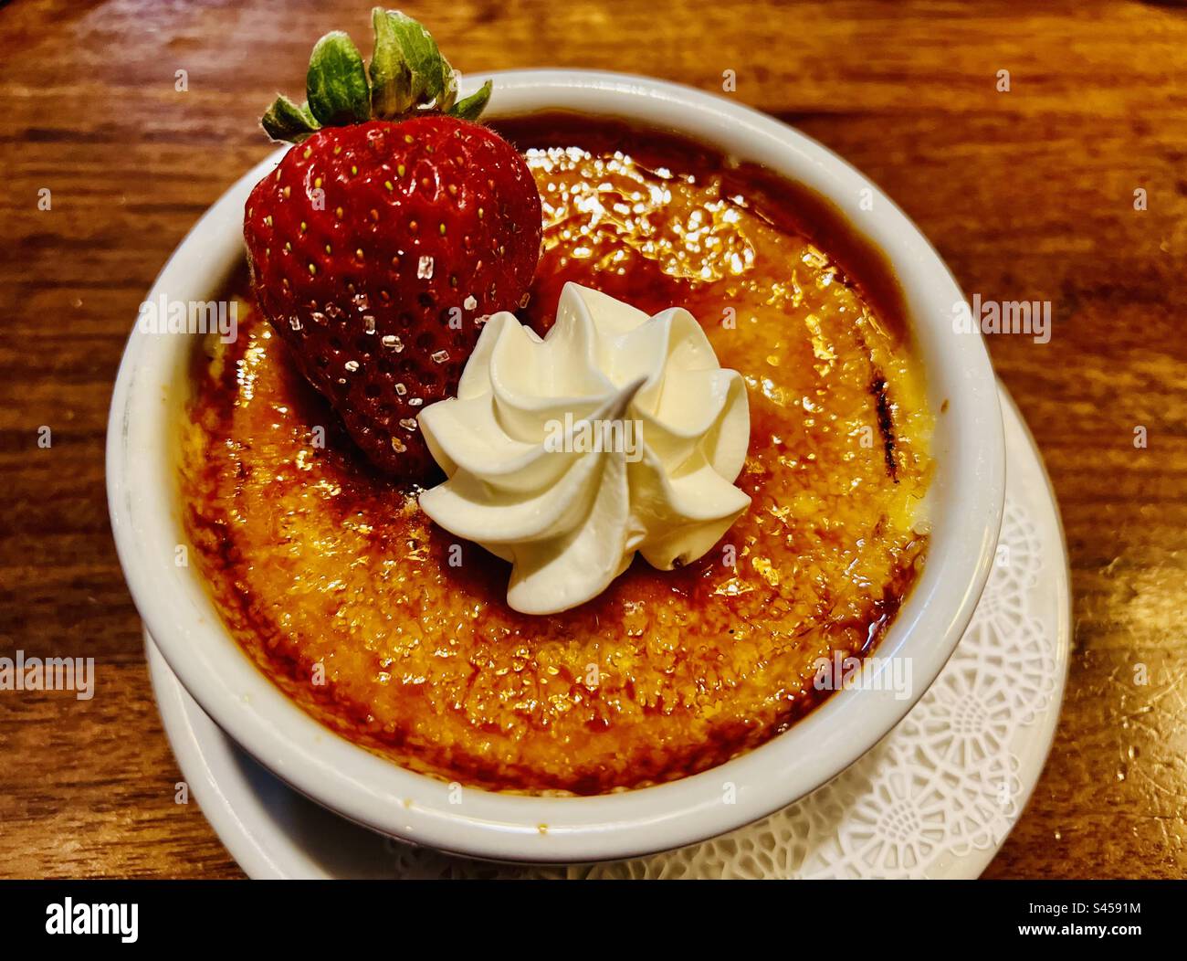 Crème brûlée mit schlagsahne und frischer Erdbeere in einem übergroßen Gericht auf einer verzogenen Holztheke. Stockfoto