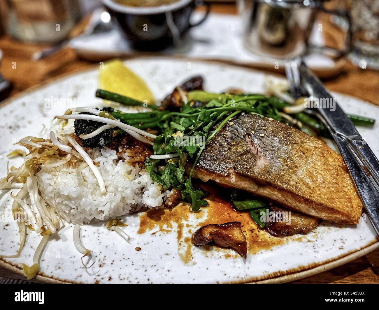 Nahaufnahme von gegrilltem Lachsfilet mit Reis, Mungbohnensprossen, Koriander und Pilzen auf dem Tisch. Konzentrieren Sie sich auf den Vordergrund. - Smartphone-aufgenommenes Stockfoto