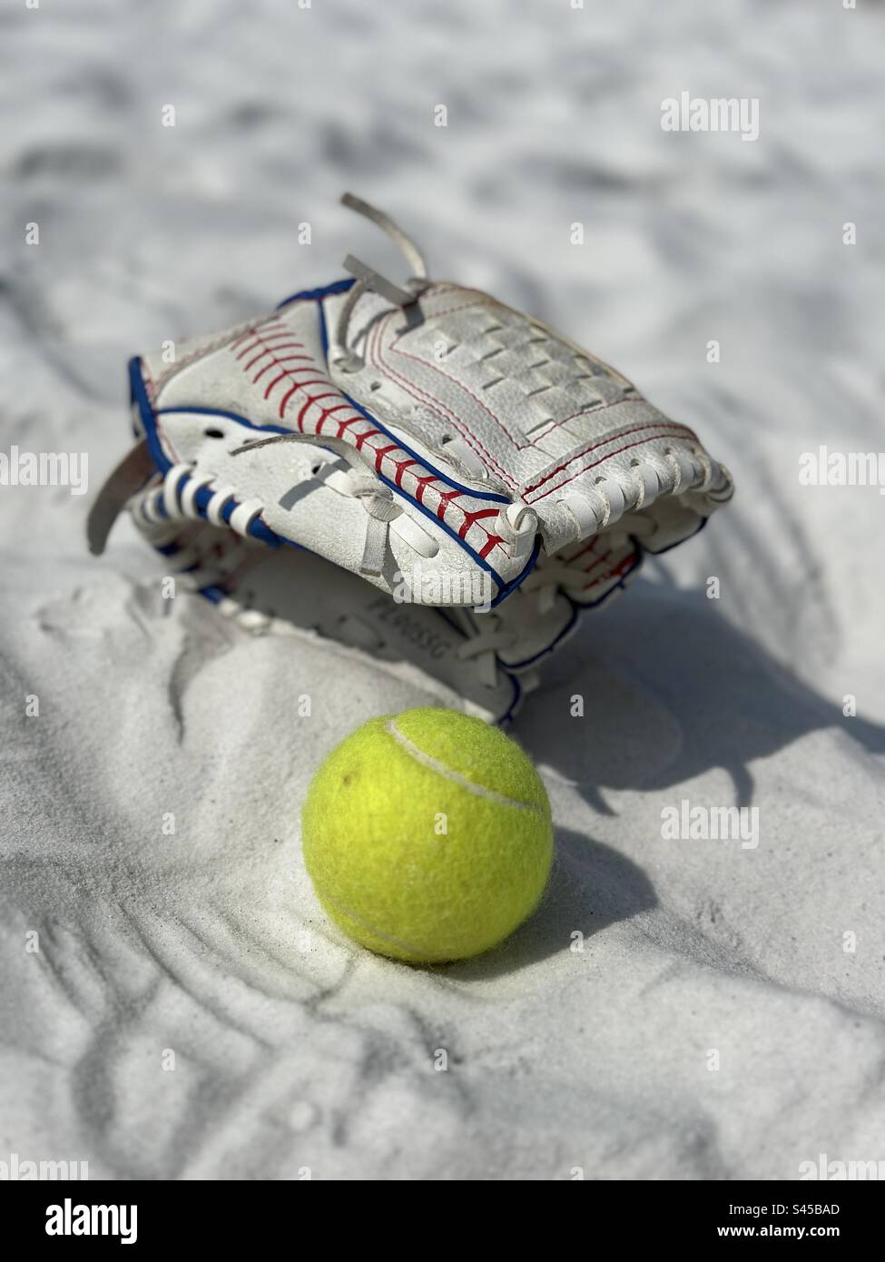 Baseballhandschuh und Ball auf weißem Sandstrand Stockfoto