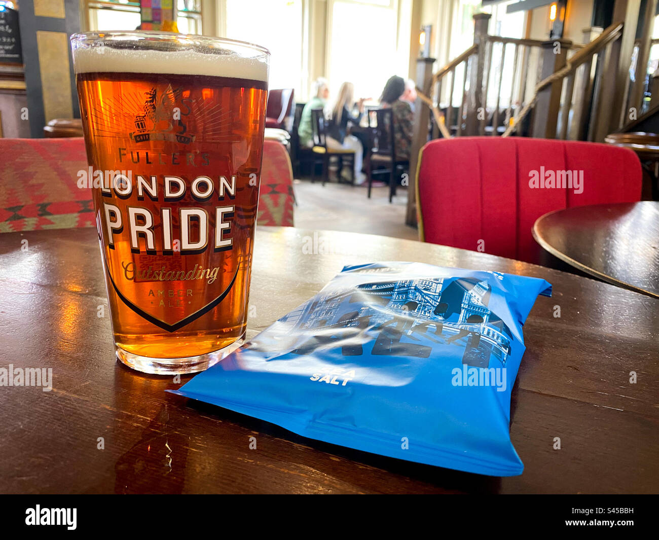 Ein Pint London Pride Bier und eine Packung Chips auf einem Tisch in einem Pub. - Smartphone-aufgenommenes Stockfoto