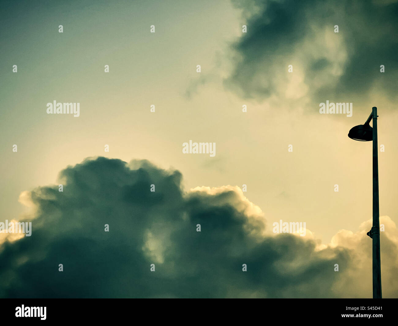 Blick aus dem niedrigen Winkel auf das Straßenlicht vor dunklen Wolken und hellem Himmel. Minimalistisch. Ruhe. Umgebung. Wind. Stockfoto