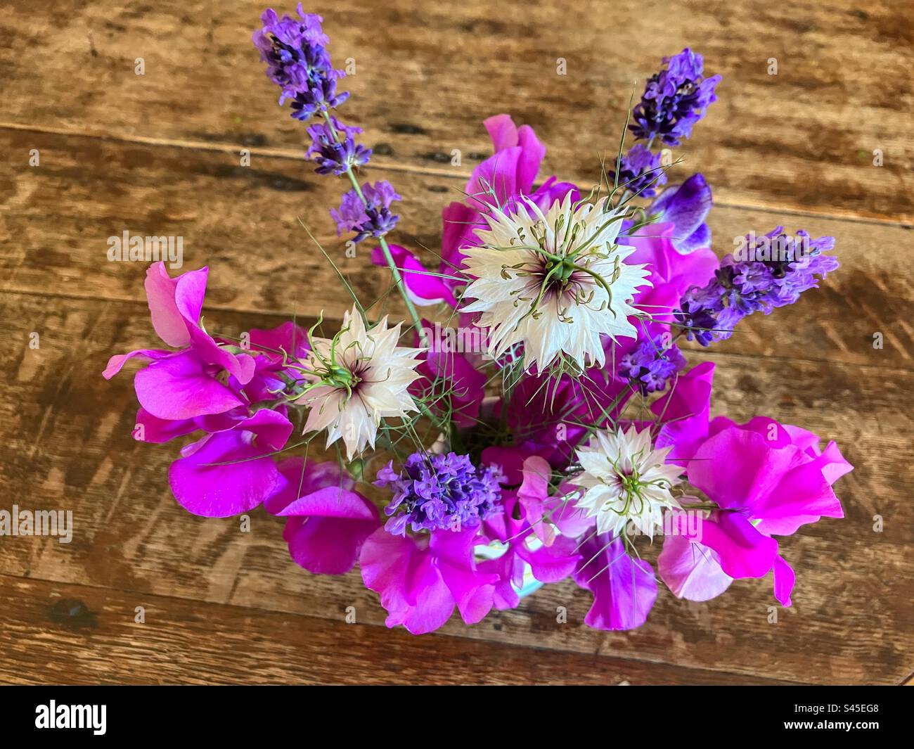 Kleiner Strauß aus rosa süßen Erbsen, lila Lavendel und weißer Liebe in einer Nebelblume in einer Vase auf einem hölzernen Tisch, von oben gesehen Stockfoto