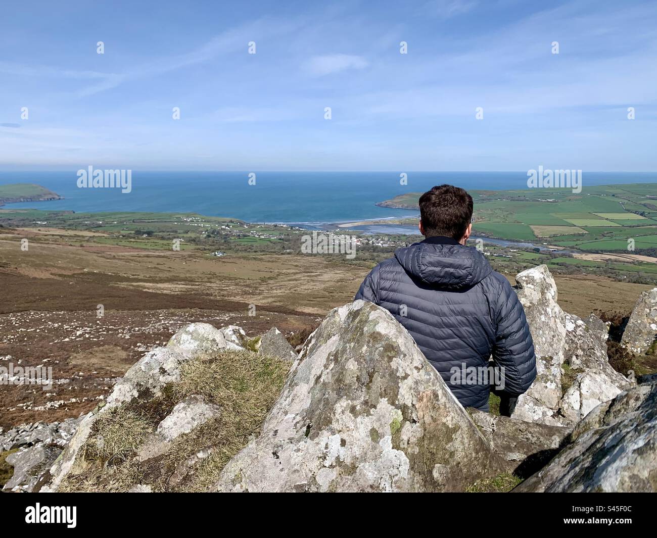 Mann sitzt auf Felsen auf dem Berg und bewundert den Blick auf das Meer über Newport Pembrokeshire Wales - Smartphone-aufgenommenes Stockfoto