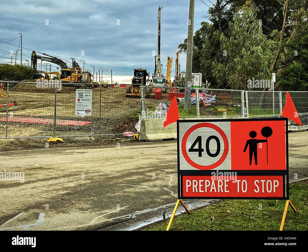 Warnschild auf dem Grasstein gegenüber der Baustelle mit schweren Maschinen. - Smartphone-aufgenommenes Stockfoto