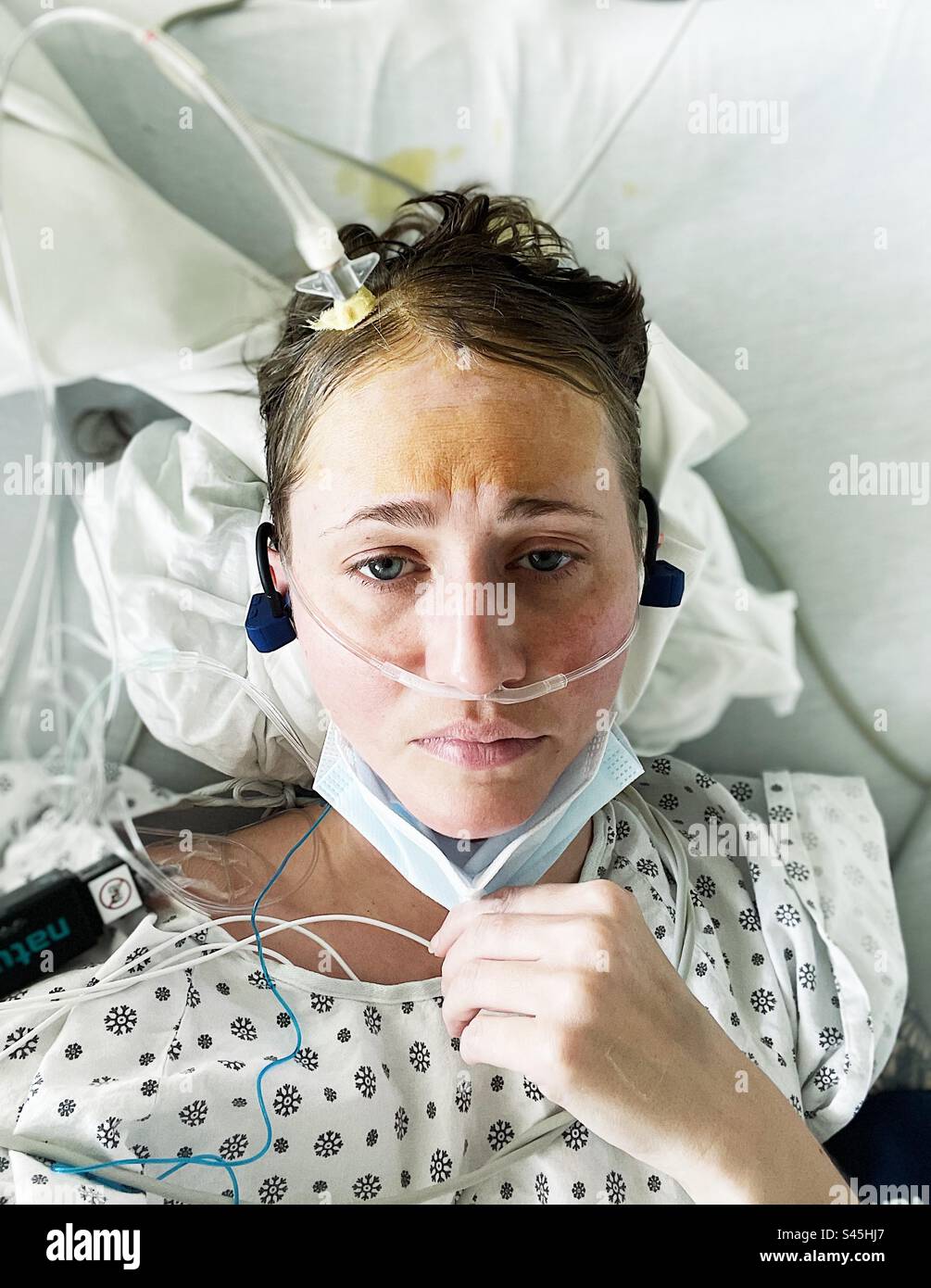 Weiblich im Krankenhauskleid mit Bolzen aus ihrem Kopf ragend, trägt eine Maske und Sauerstoff Stockfoto