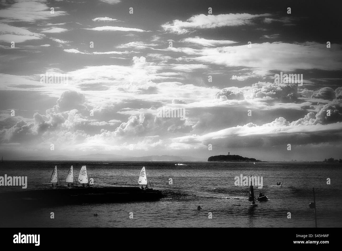 Einige Segelboote segeln ruhig über das Foto. Die Insel Enoshima ist im Hintergrund. Stockfoto