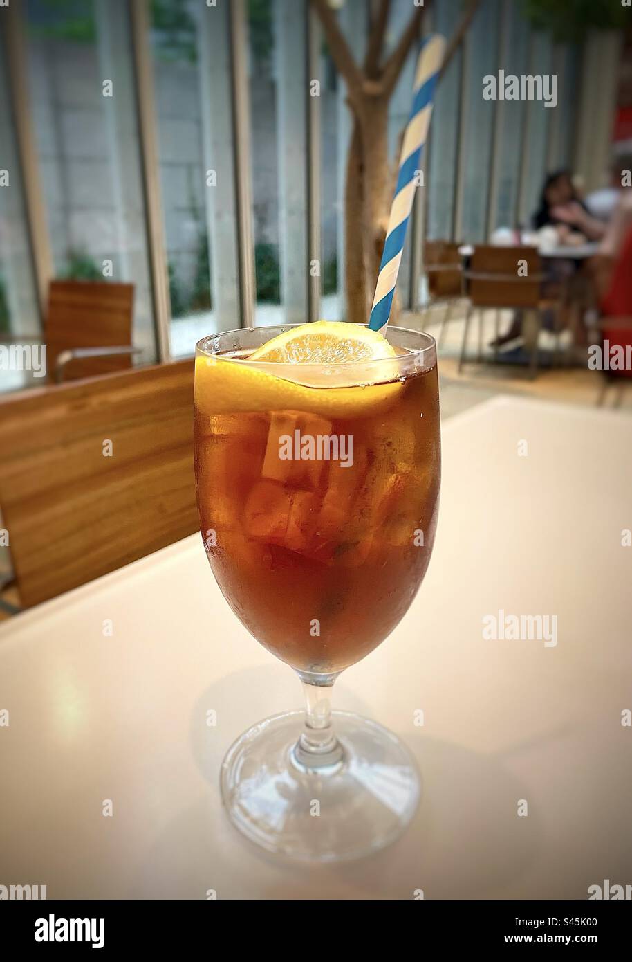 Ein blau-weiß gestreifter Strohhalm in einem Glas Eistee mit Zitrone Stockfoto