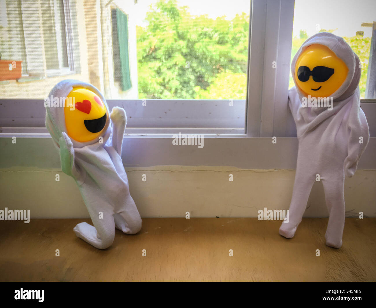 Eine Puppe kniet in Liebe vor der anderen schönen Puppe. Darstellung einer Verliebtheitssituation mit Puppen mit Emoticon-Gesichtern. - Smartphone-aufgenommenes Stockfoto