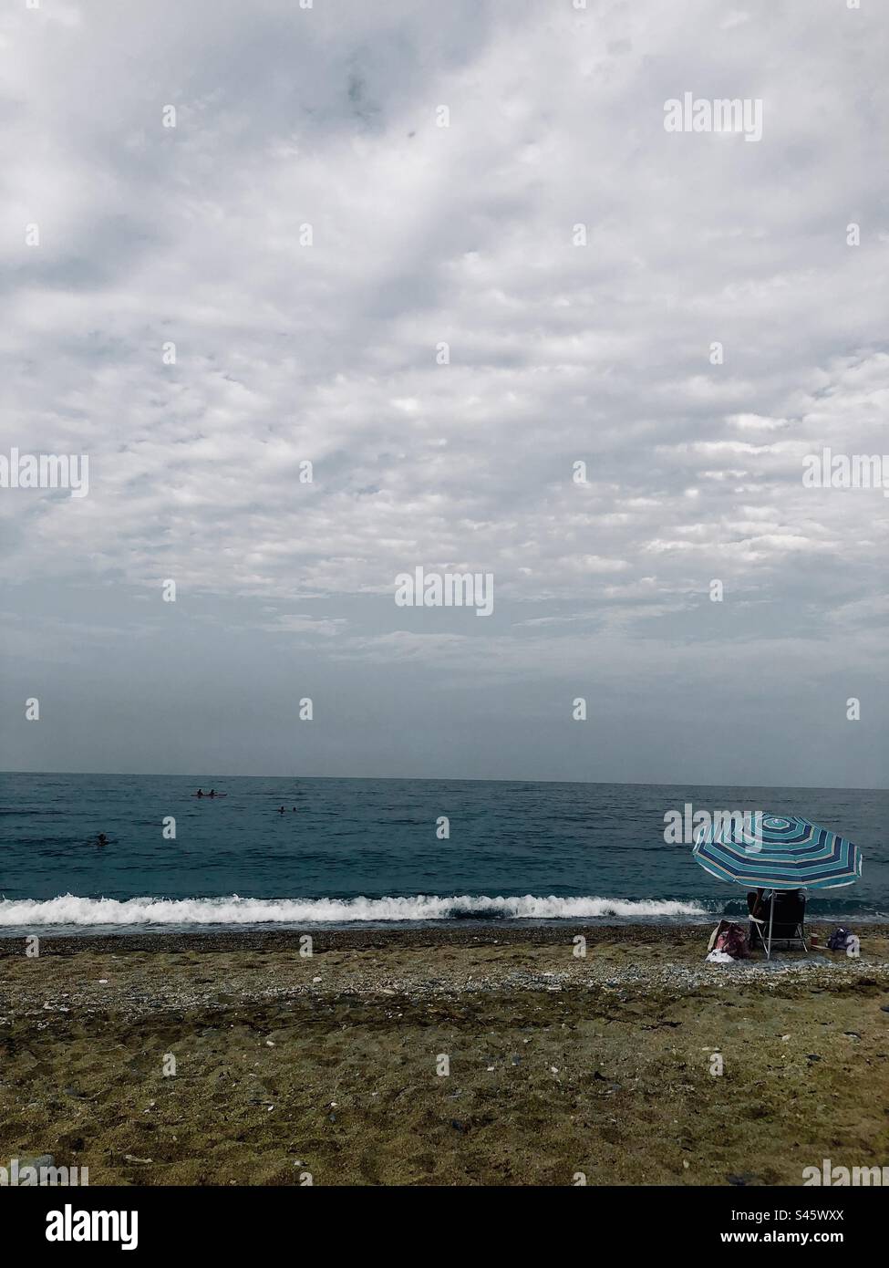 Mann unter blauem Schirm und bewölkter Himmel am Meer - Smartphone-aufgenommenes Stockfoto