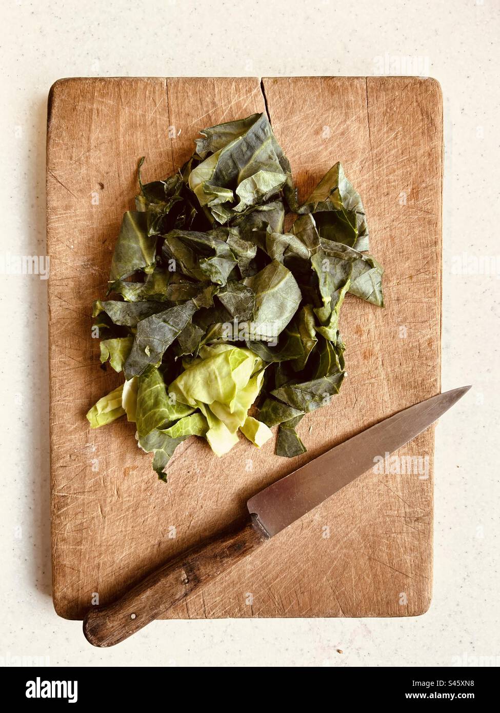 Gehackter grüner Kohl und ein Küchenmesser mit Holzgriff auf einem Schneidebrett. Fertig zum Kochen. - Smartphone-aufgenommenes Stockfoto