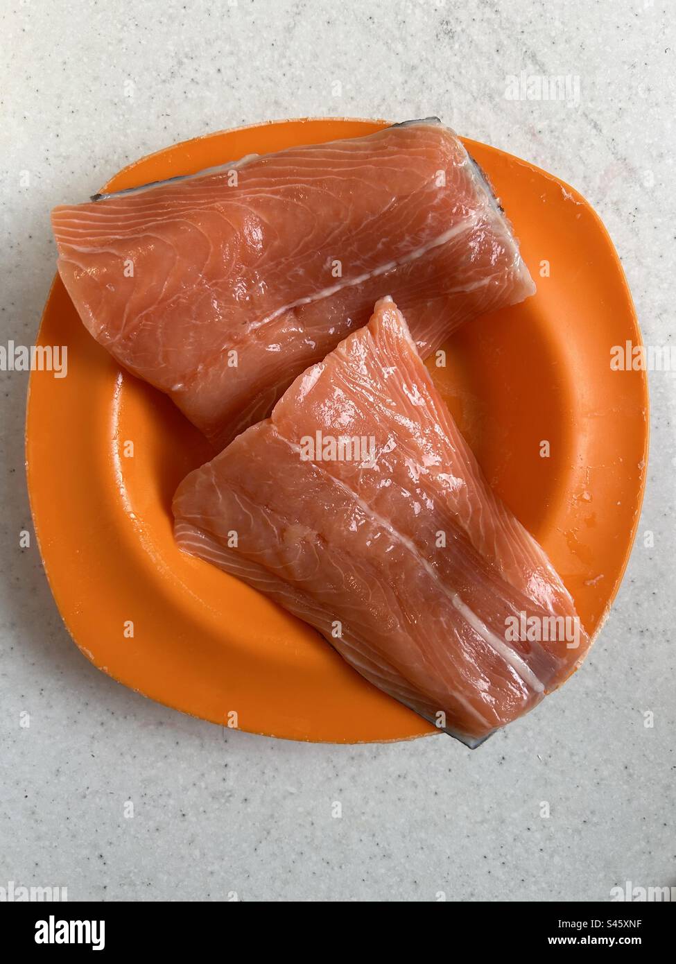 Frische Lachsschwänze auf einem orangefarbenen Teller. Fertig zum Kochen. Stockfoto