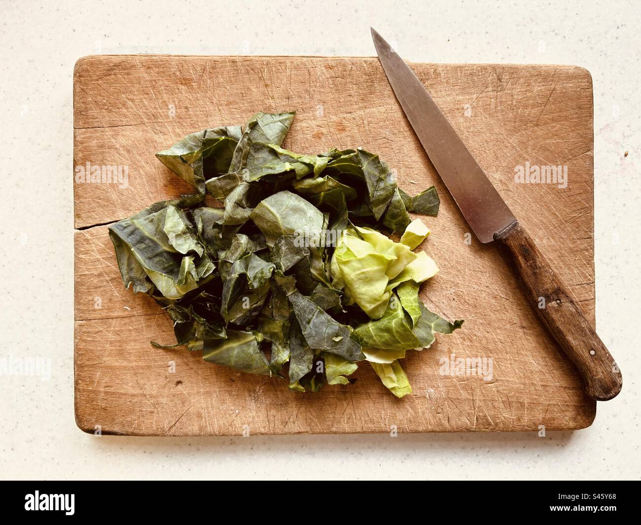 Gehackter grüner Kohl und Küchenmesser mit Holzgriff auf zerbrochenem alten Holzbrett. Fertig zum Kochen. Bereit zum Salat. - Smartphone-aufgenommenes Stockfoto