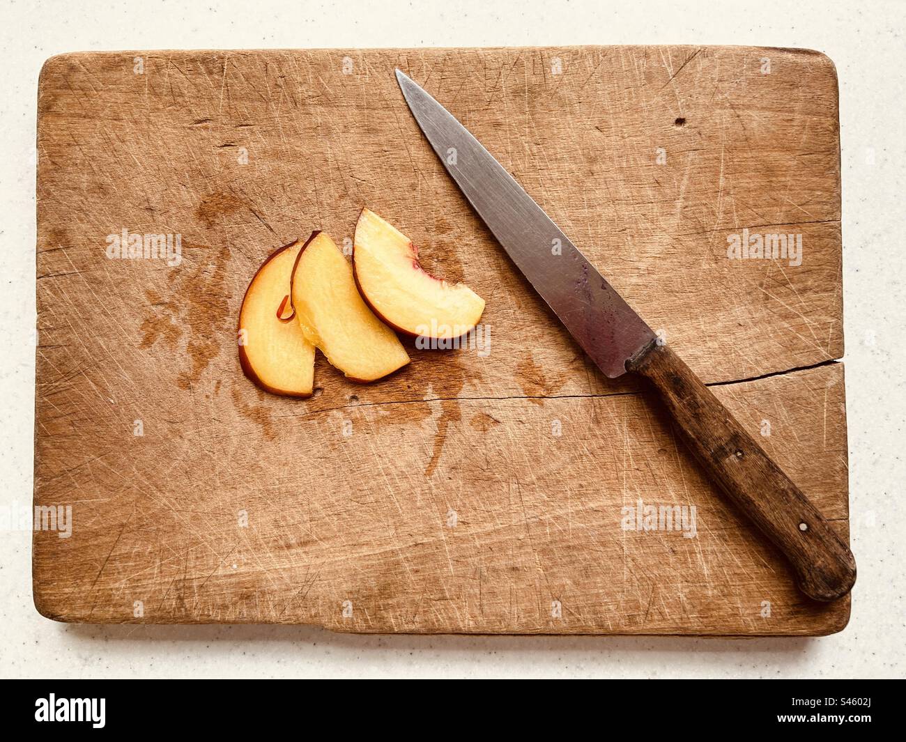 Drei Nektarinscheiben und ein Küchenmesser auf einem alten nassen Holzhacke. - Smartphone-aufgenommenes Stockfoto