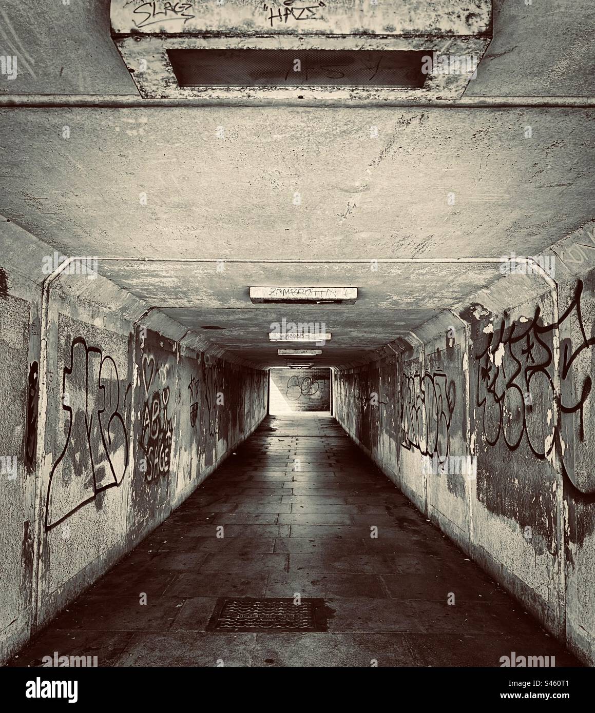 Eine U-Bahn sieht nicht einladend aus - dunkel, feucht und heruntergekommen. Graffiti-besprühte Wände befinden sich auf beiden Seiten des Gangs. (Schwarzweiß) Stockfoto