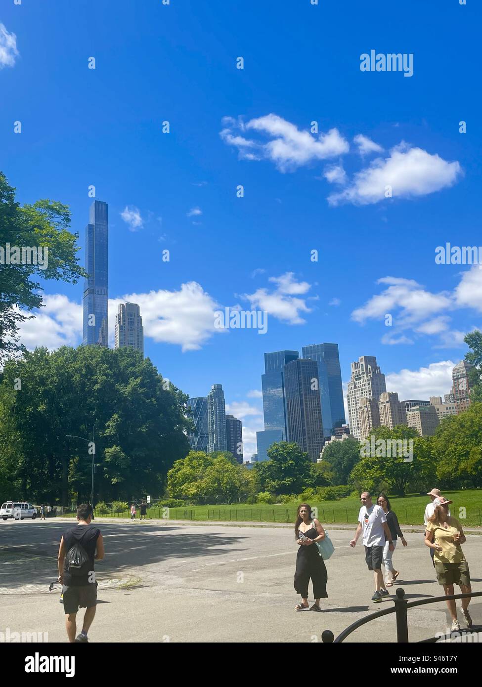 Menschen, die im Sommer durch den Central Park spazieren, mit Blick auf Wolkenkratzer im Hintergrund, New York City Stockfoto