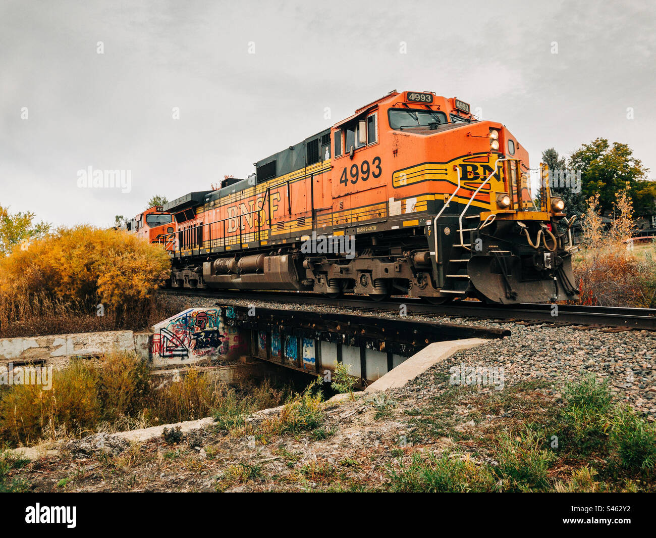 Eine BNSF-Lokomotive zieht einen Güterzug über eine kleine Brücke in herbstlicher Landschaft. Stockfoto