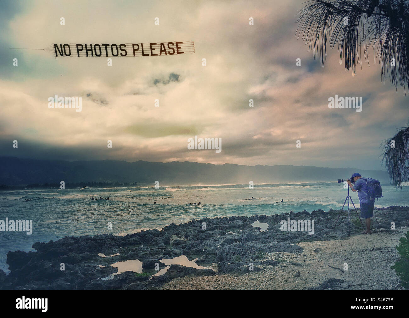 Ein Mann fotografiert Surfer mit einem Flugzeug-Banner, auf dem "BITTE KEINE FOTOS" über dem Kopf steht - Smartphone-aufgenommenes Stockfoto