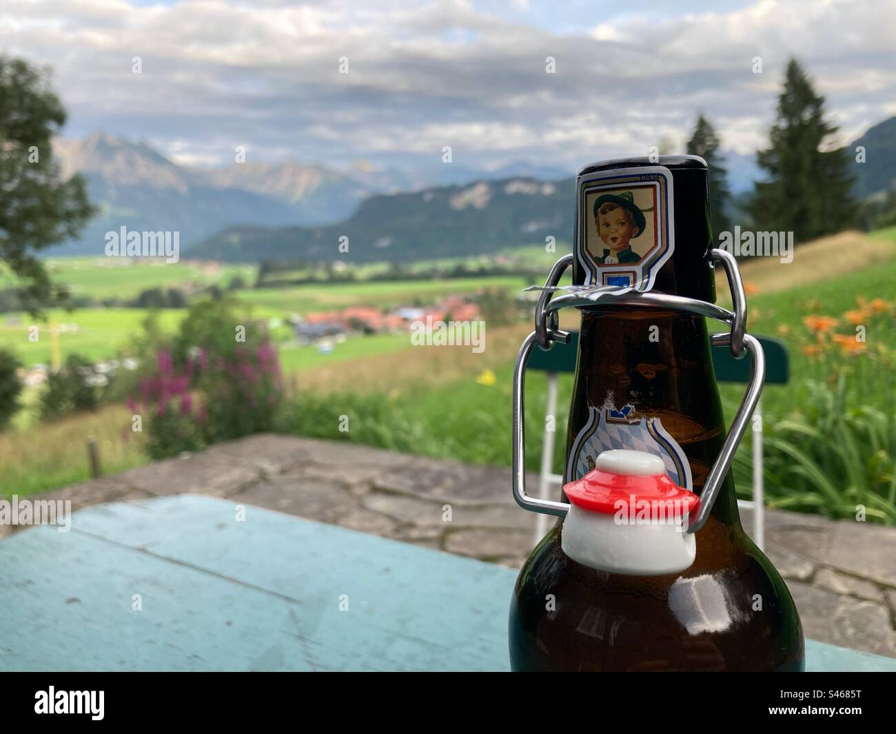 Ein offenes Bier auf einem grünen Holztisch mit den deutschen Alpen im Hintergrund Stockfoto