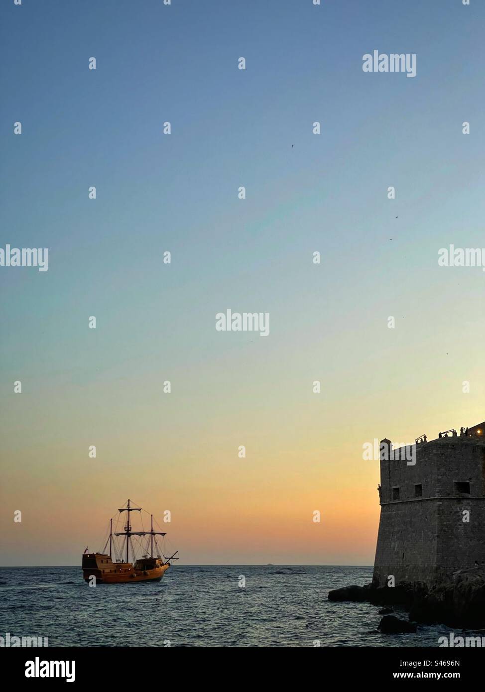 Boot im Game of Thrones-Stil, das in der Dämmerung an den Mauern von Dubrovnik (Königslandung), Kroatien, vorbeifährt. Stockfoto