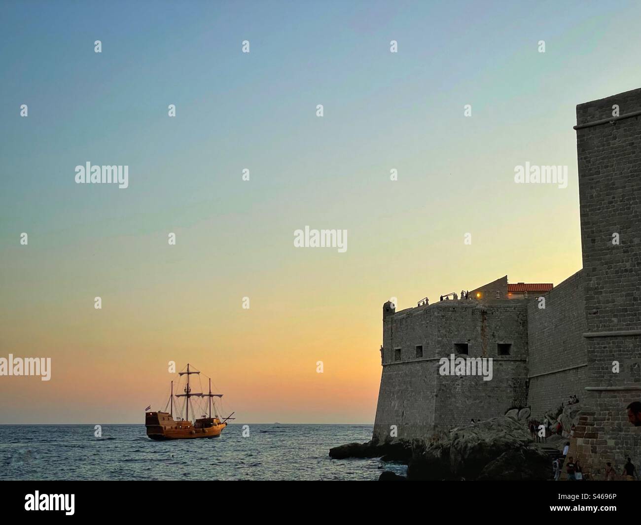 Ein Schiff im Stil von Game of Thrones, das in der Abenddämmerung an den Mauern der Altstadt von Dubrovnik (auch bekannt als King’s Landing in der HBO-Serie) in Kroatien vorbeisegelt. Stockfoto