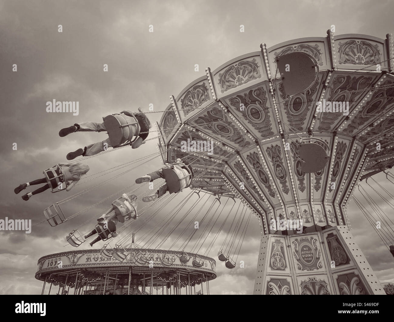 Kinder genießen den Nervenkitzel einer schnellen, rotierenden Fahrt namens Sky Swinger. Eine lustige Fahrt, die Erinnerungen an vergangene Zeiten zurückbringt. Foto ©️ COLIN HOSKINS. - Smartphone-aufgenommenes Stockfoto