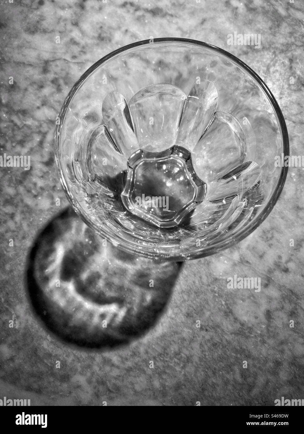 Ein Blick von oben auf ein kleines Trinkglas. Ein interessanter Schatten entsteht durch die Verwendung eines Scheinwerfers auf einem Marmortisch. Foto ©️ COLIN HOSKINS. Stockfoto