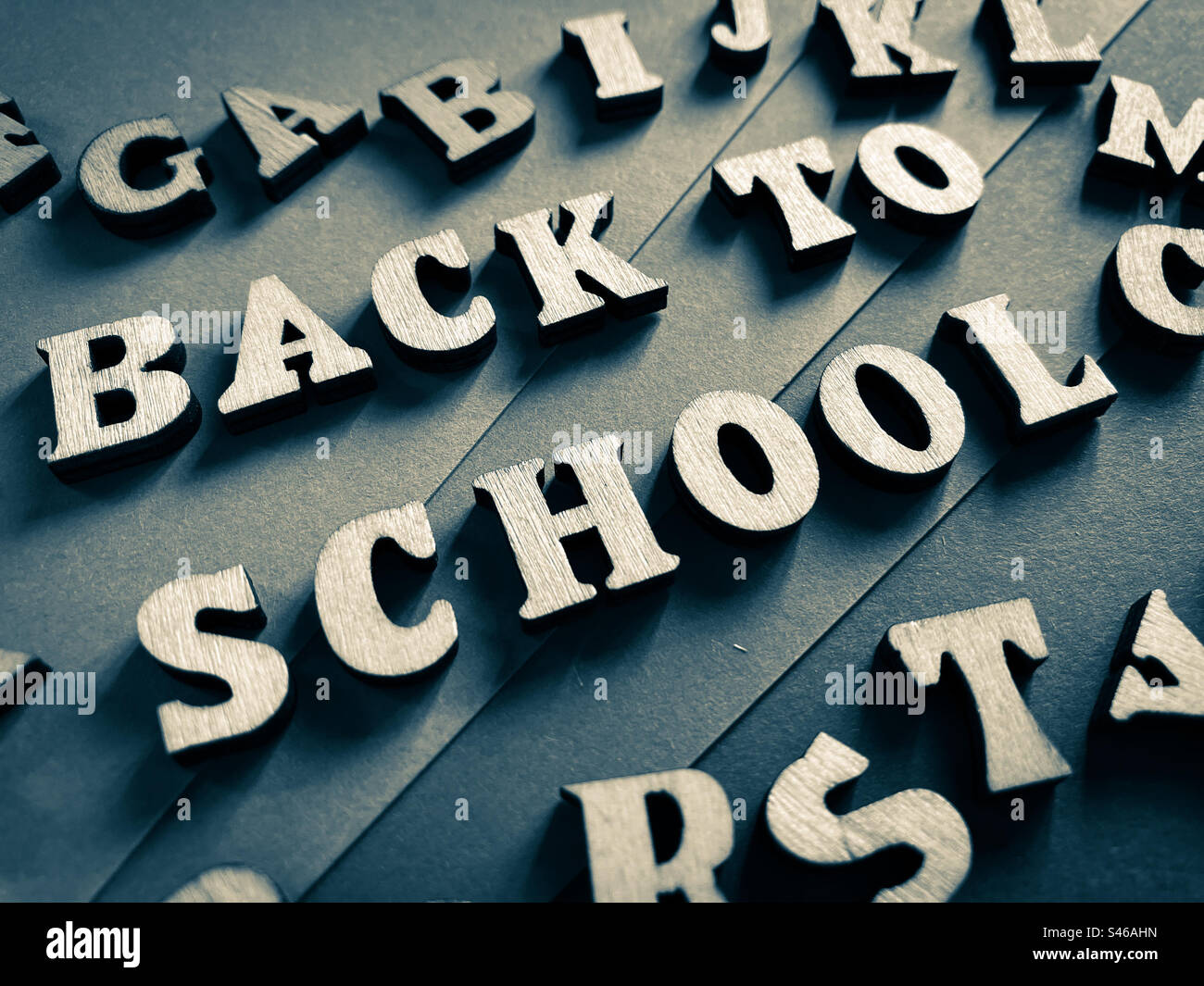 Zurück zur Schule, Wörter in hölzernen Buchstaben, umgeben von zufälligen Buchstaben, isoliert auf grauem Hintergrund Stockfoto