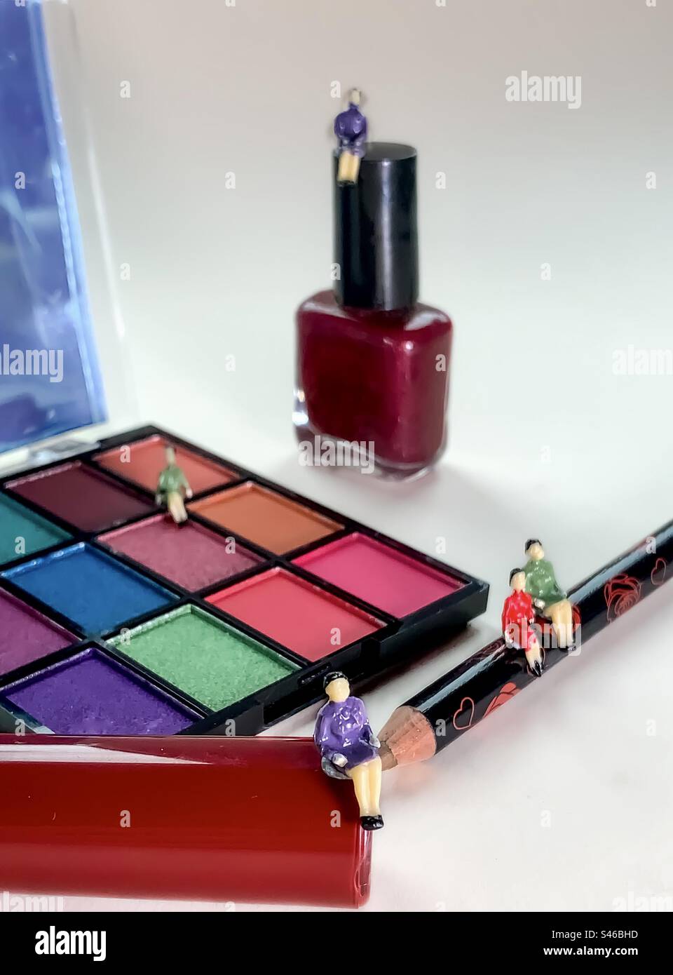 Miniaturfiguren sitzen auf verschiedenen Kosmetikartikeln - Smartphone-aufgenommenes Stockfoto
