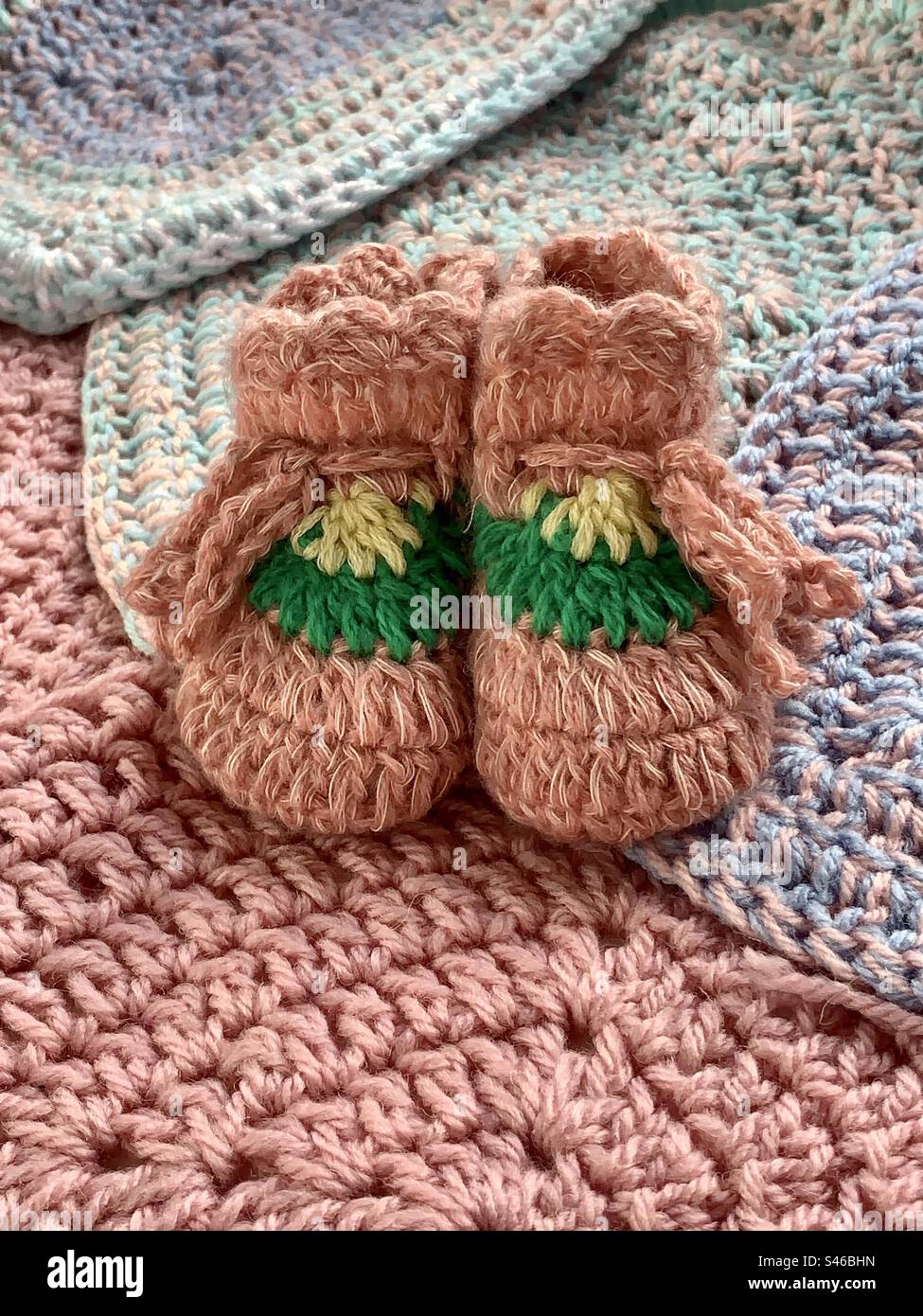 Pinke gestrickte Babyschühchen auf einem Hintergrund aus gestrickten Quadraten - Smartphone-aufgenommenes Stockfoto