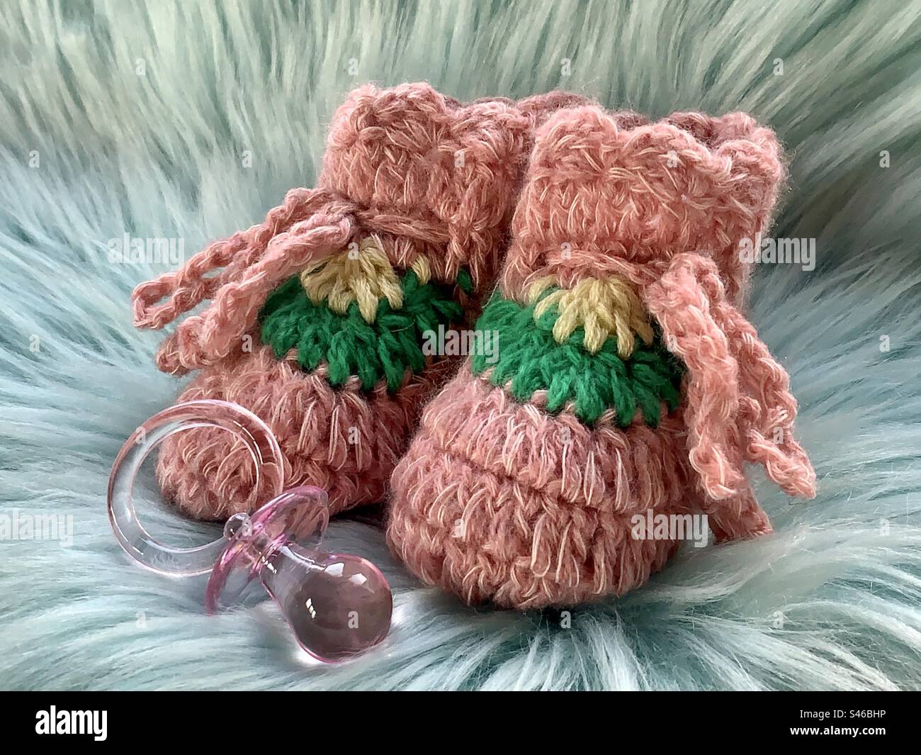 Pinke gestrickte Babyschühchen auf einem Hintergrund aus Kunstfell - Smartphone-aufgenommenes Stockfoto