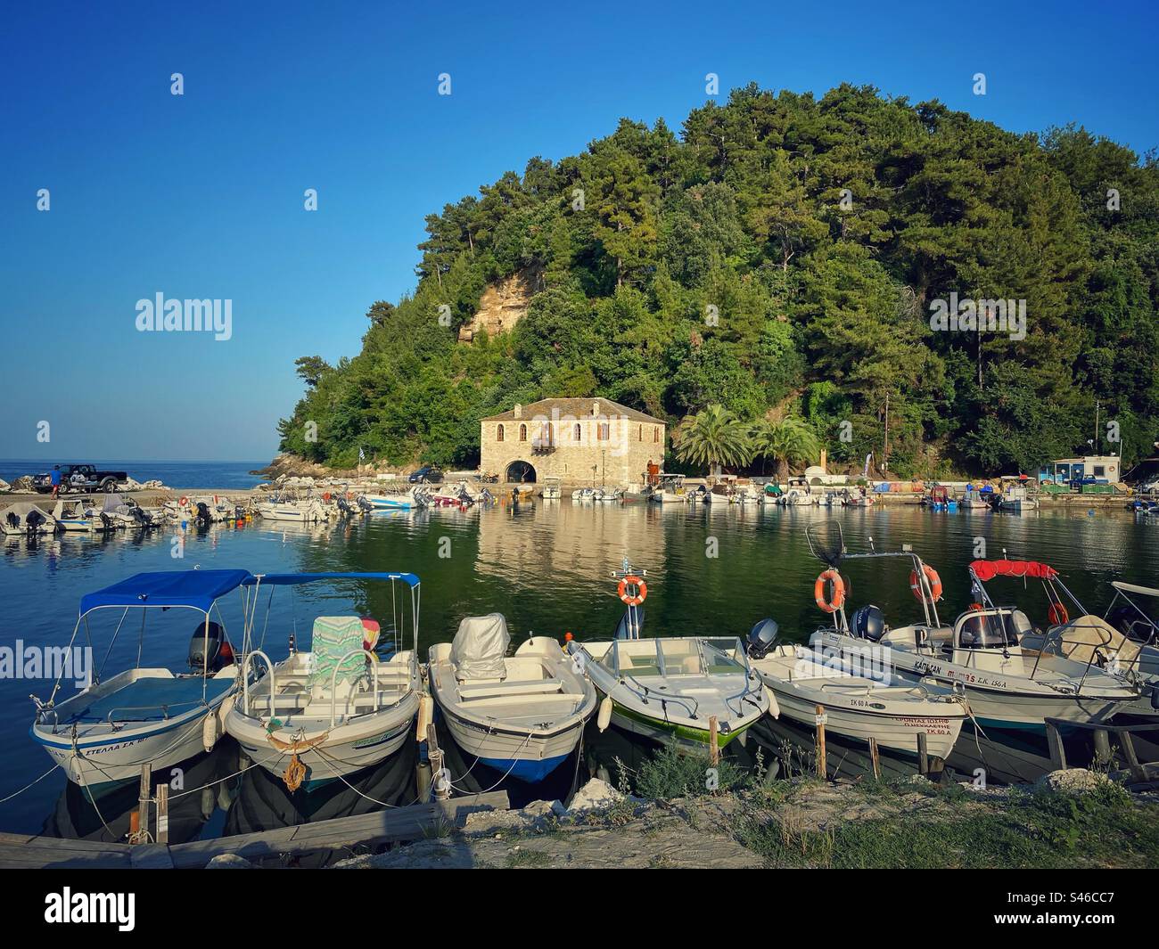 Alter Hafen mit Booten bei Sonnenuntergang mit grünem Hügel im Hintergrund in Skala Potamias, Thassos Insel, Griechenland. - Smartphone-aufgenommenes Stockfoto