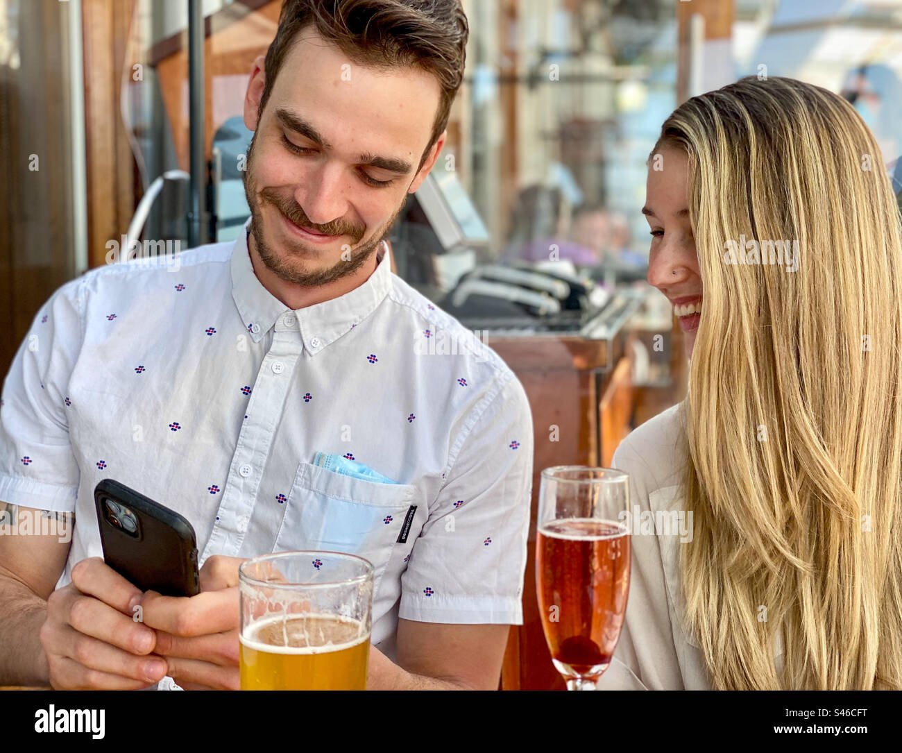 Junger Mann und Frau, die in einem Restaurant auf das Handy schauen. - Smartphone-aufgenommenes Stockfoto