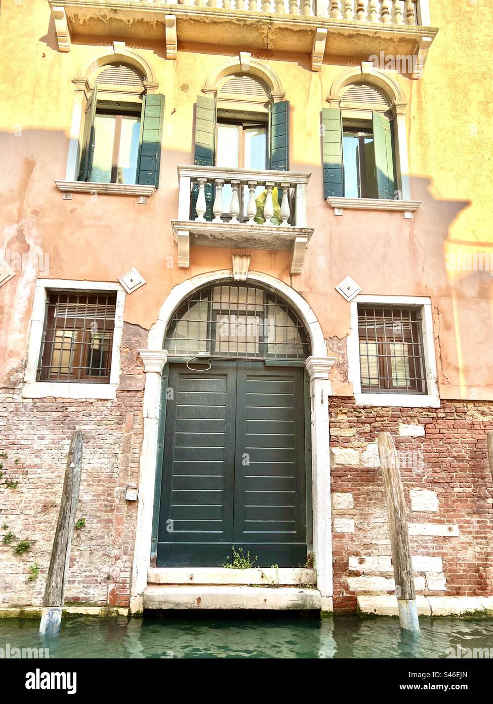 Kanalhaus mit rosa und gelben Tönen auf Stein mit roten Ziegeln und einem grünen Türakzent in Rio di San Felipe, Cannaregio Viertel, Venedig Stockfoto