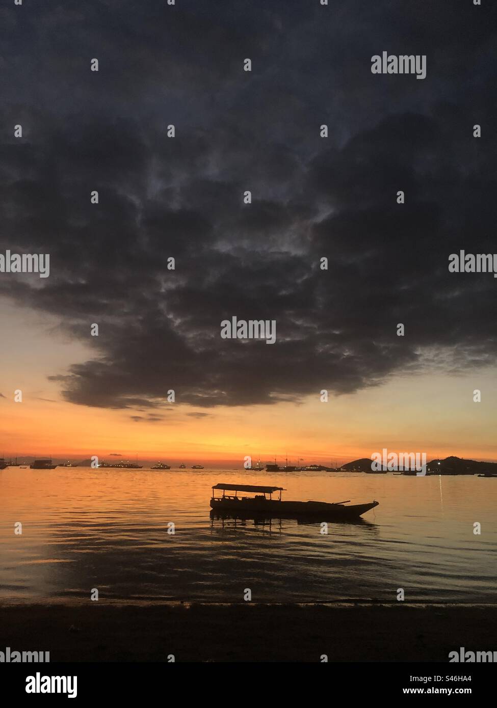 Golden Horizons: Fangen Sie die ruhige Schönheit des Sonnenuntergangs am Strand ein, wo das Boot seinen ruhigen Ort findet. Stockfoto