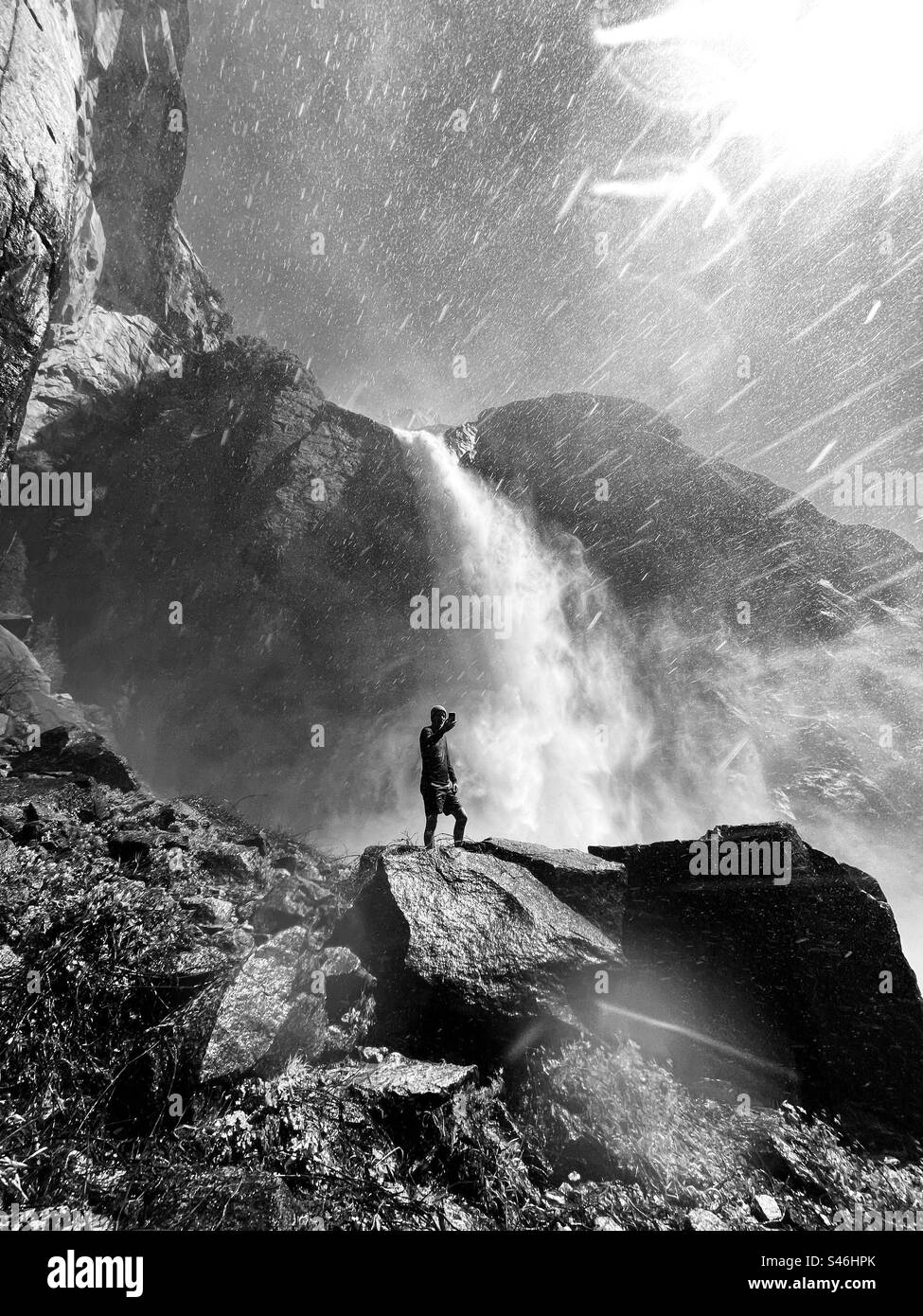 Der Wanderer nimmt ein Selfie unter den Lower Yosemite Falls. Kalifornien verzeichnete einen der größten Schneefälle im Jahr 2023, der im Juli 2023 im Yosemite National Park, Kalifornien, USA, zu vollständig fließenden Wasserfällen führte. Stockfoto