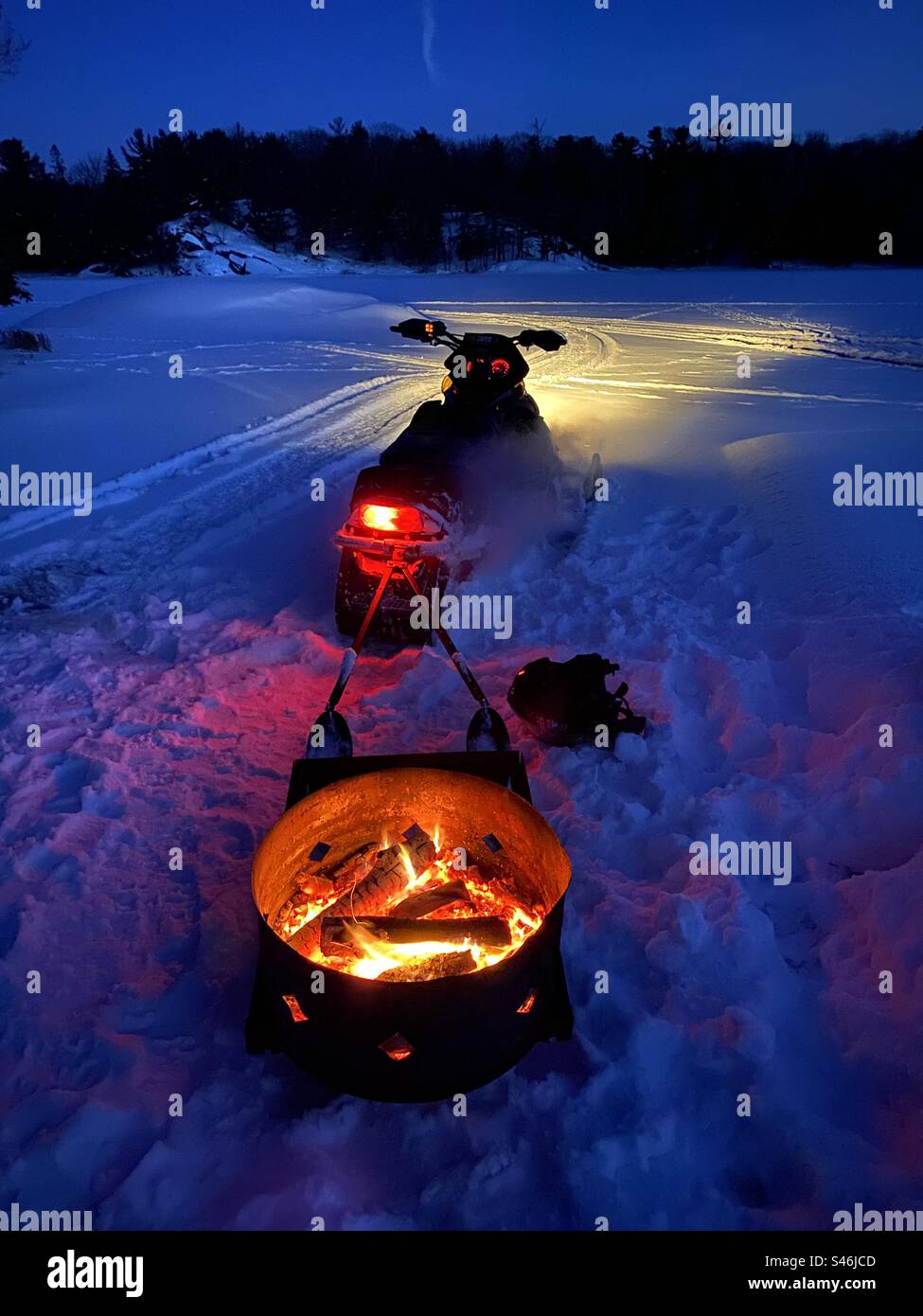 Schneemobil, das nachts eine Feuerstelle über einen verschneiten See zieht. Stockfoto