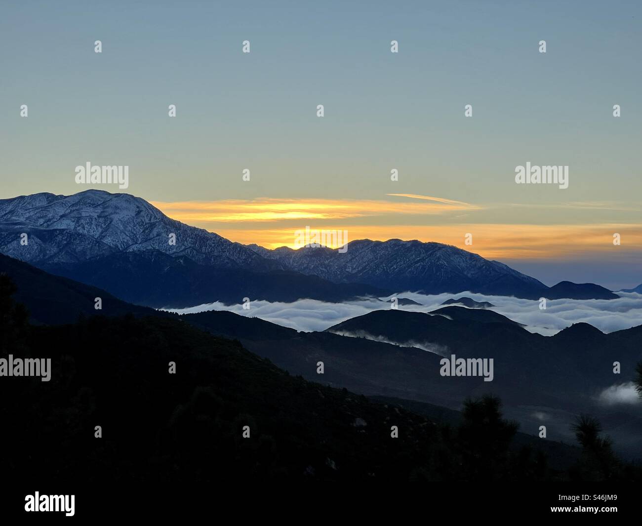 Berge mit niedrigen Wolken, die sich bei Sonnenuntergang unter den silhouettierten Gipfeln abrollen Stockfoto