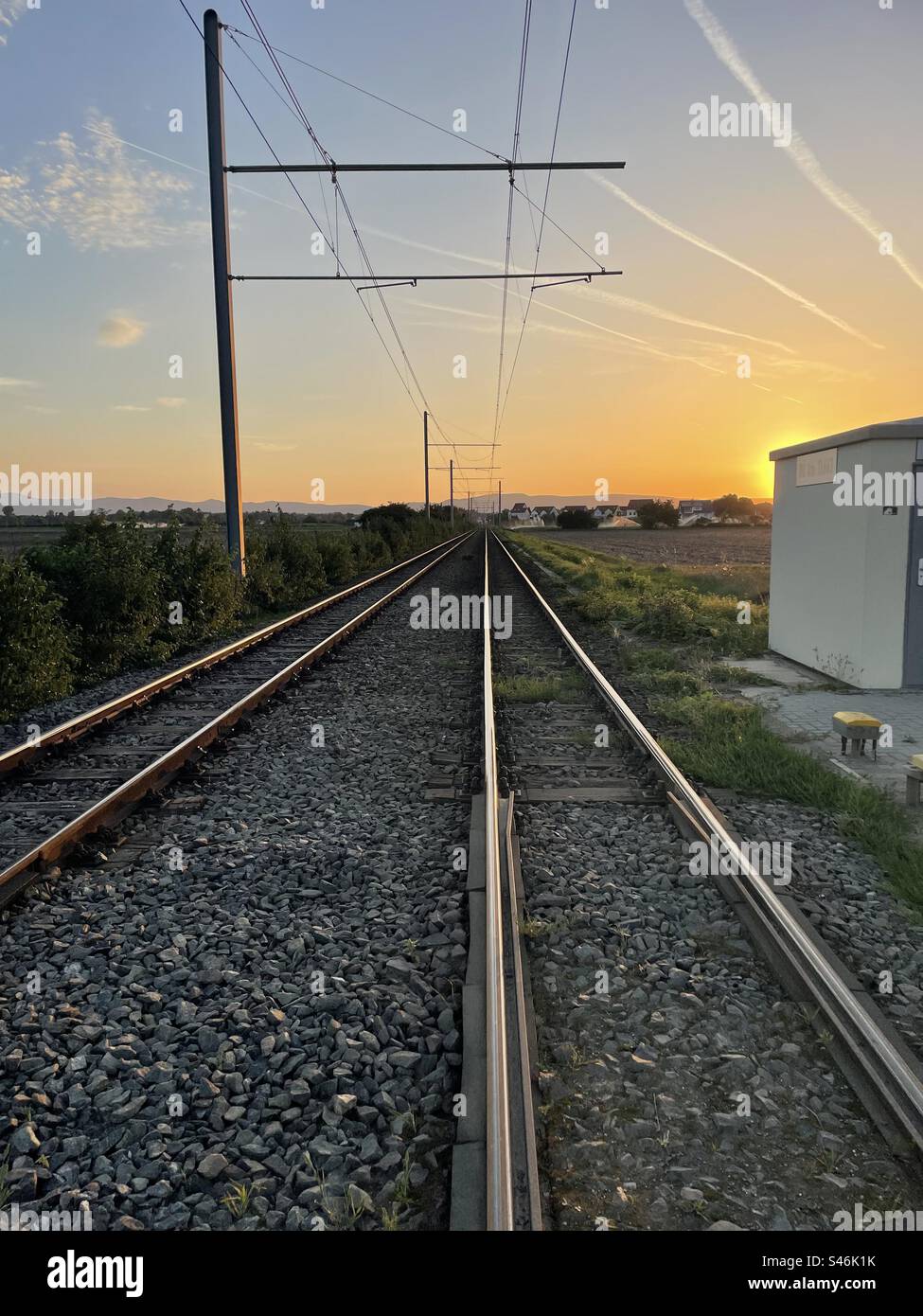 Während die Sonne untergeht, verblassen Eisenbahnschienen in die Ferne, während der Himmel über den Flugzeugen die flüchtigen Spuren trägt, die auf die dynamische Bewegung der Welt hinweisen. Stockfoto