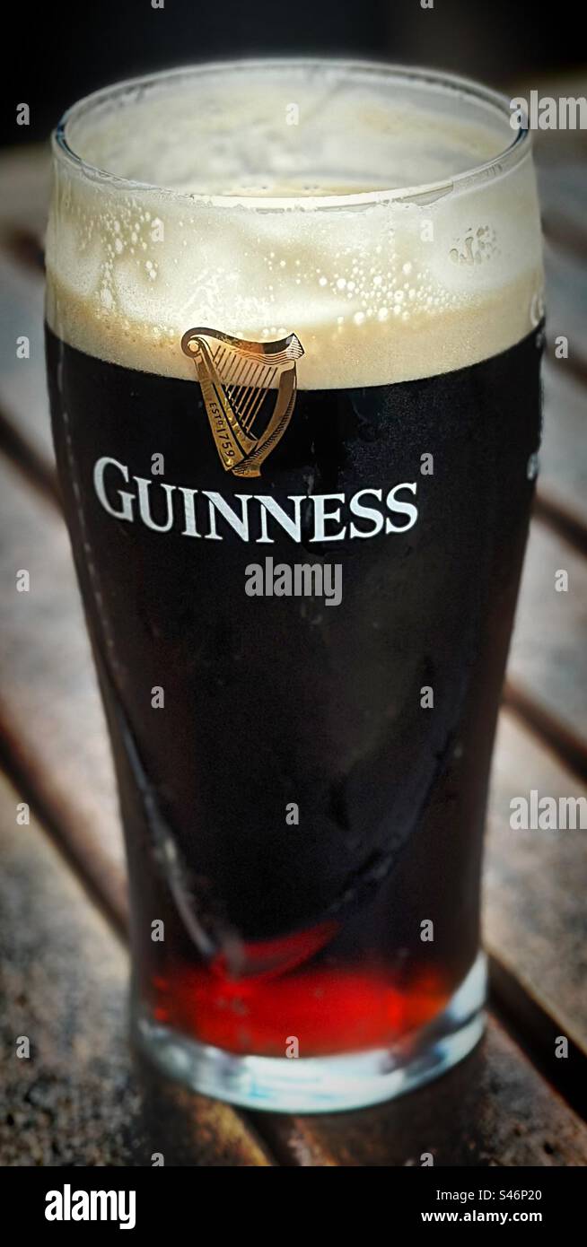 „Irlands feinstes“ ein Pint Guinness, frisch gegossen mit einem köstlichen Geschmack, der bereits auf einer Biergartenbank genossen wird. Stockfoto